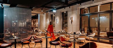 A modern interior with a mix of seating arrangements, including round tables and chairs, and a large glass wall offering a view.