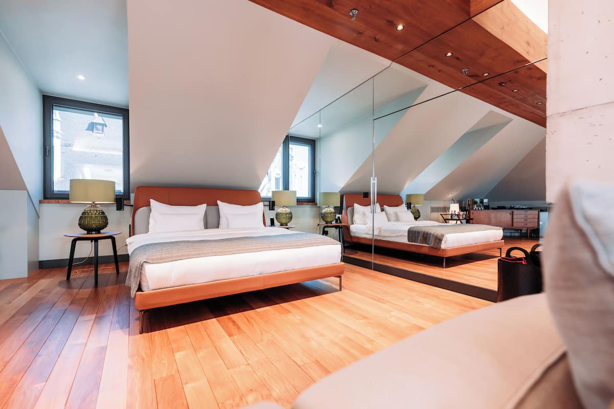 A modern bedroom with a large bed, a small bedside table, and a mirror on the wall.