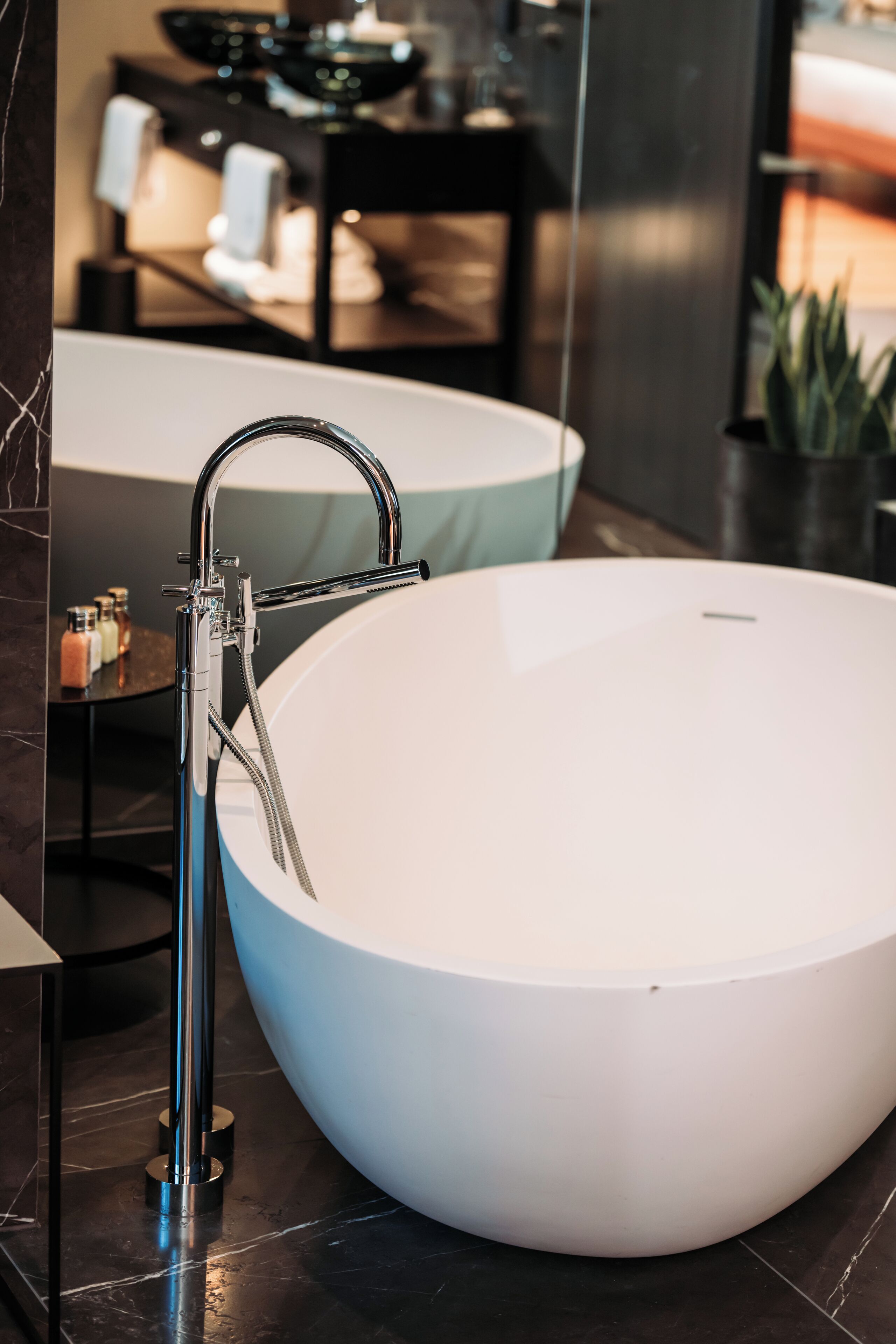 Un baño moderno con una bañera blanca grande, un grifo de cromo elegante y una mesita de noche con artículos de aseo.