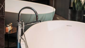 Un baño moderno con una bañera blanca grande, un grifo de cromo elegante y una mesita de noche con artículos de aseo.