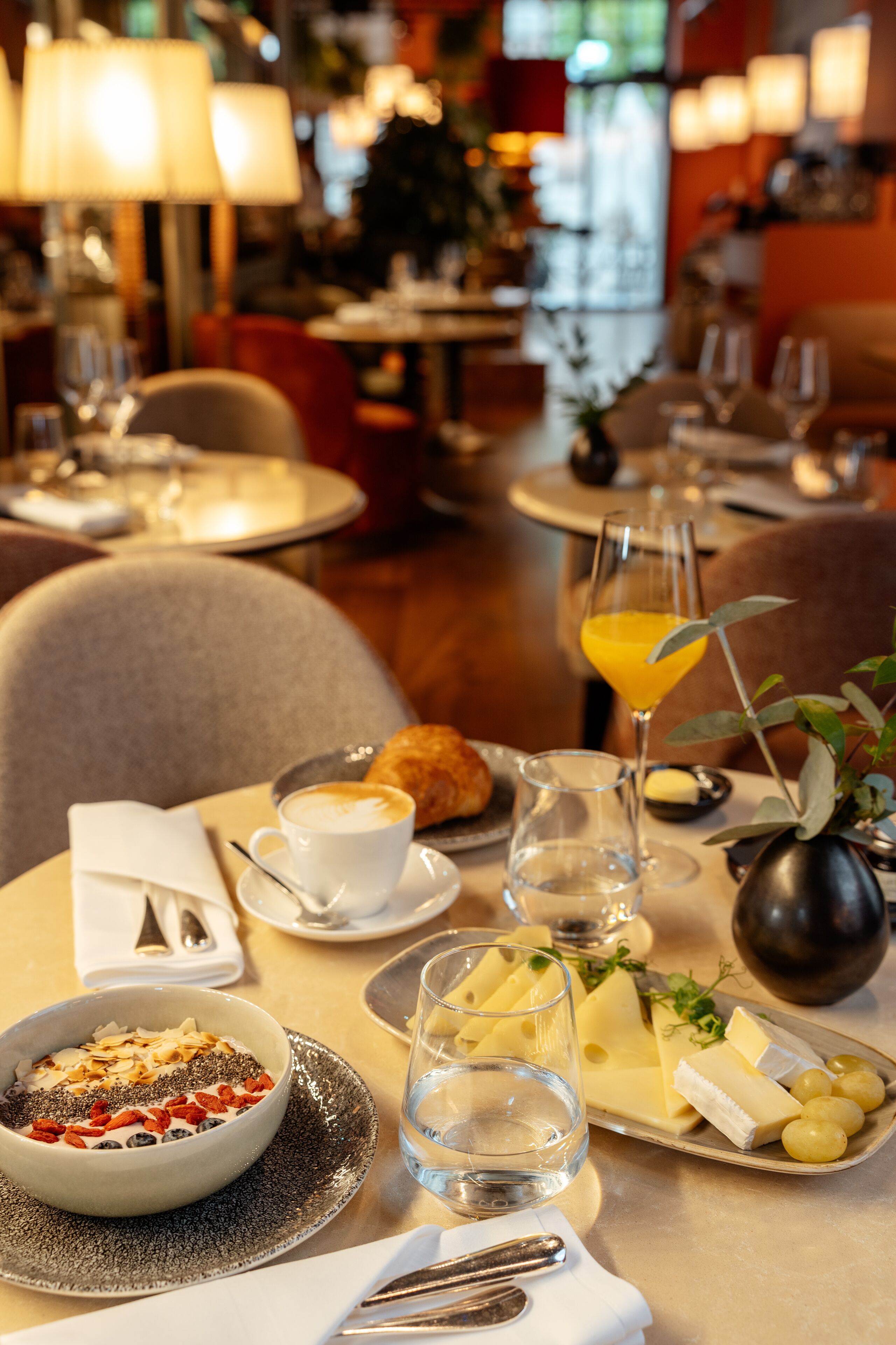 Ein Esstisch, gedeckt mit Frühstücksartikeln, darunter eine Schüssel mit Müsli, ein Glas Orangensaft und ein Teller mit Käse und Trauben.