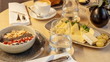 Ein Esstisch, gedeckt mit Frühstücksartikeln, darunter eine Schüssel mit Müsli, ein Glas Orangensaft und ein Teller mit Käse und Trauben.