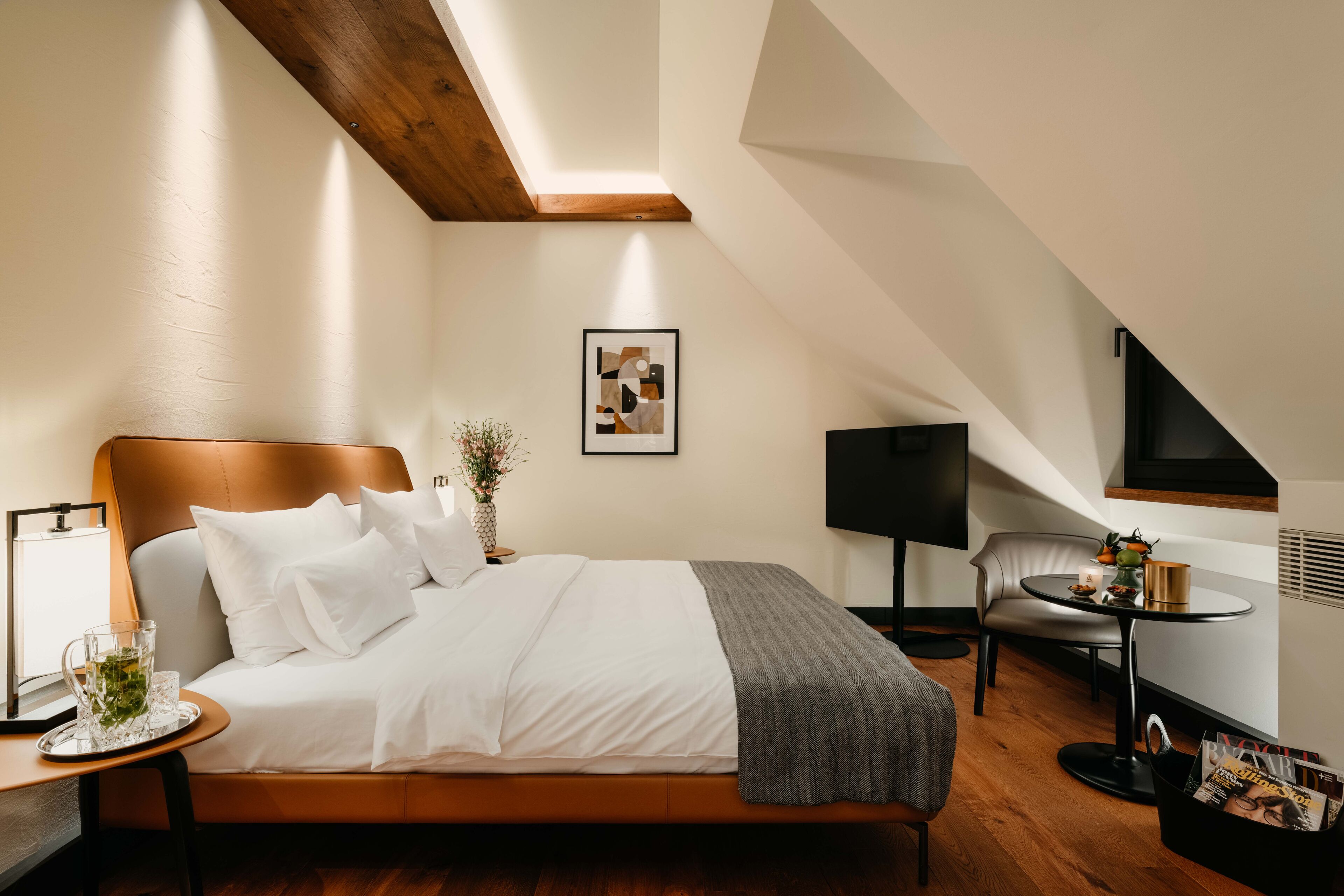 Una camera d'albergo moderna con un grande letto, un comodino con una lampada, un tavolino con un vaso, un quadro appeso alla parete e un televisore su un mobile.