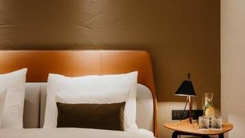 A neatly made bed with white and brown bedding, a wooden headboard, and a small bedside table with a lamp and glasses.