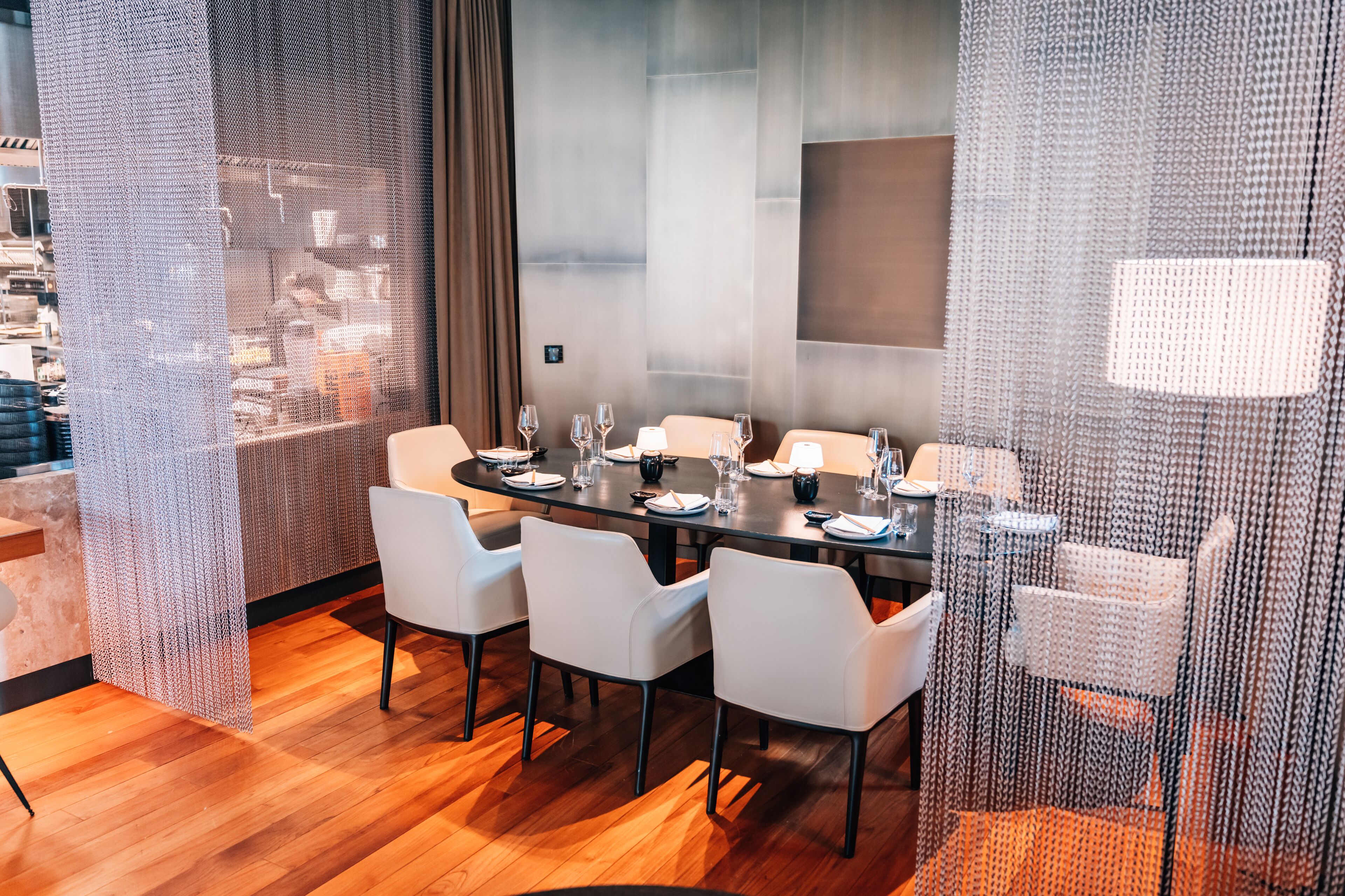 A modern dining area with a long table set for six, surrounded by white chairs.