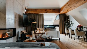 A modern loft bedroom with a fireplace, a dining area, and a view of the city. - DO & CO Hotel München (Munich)