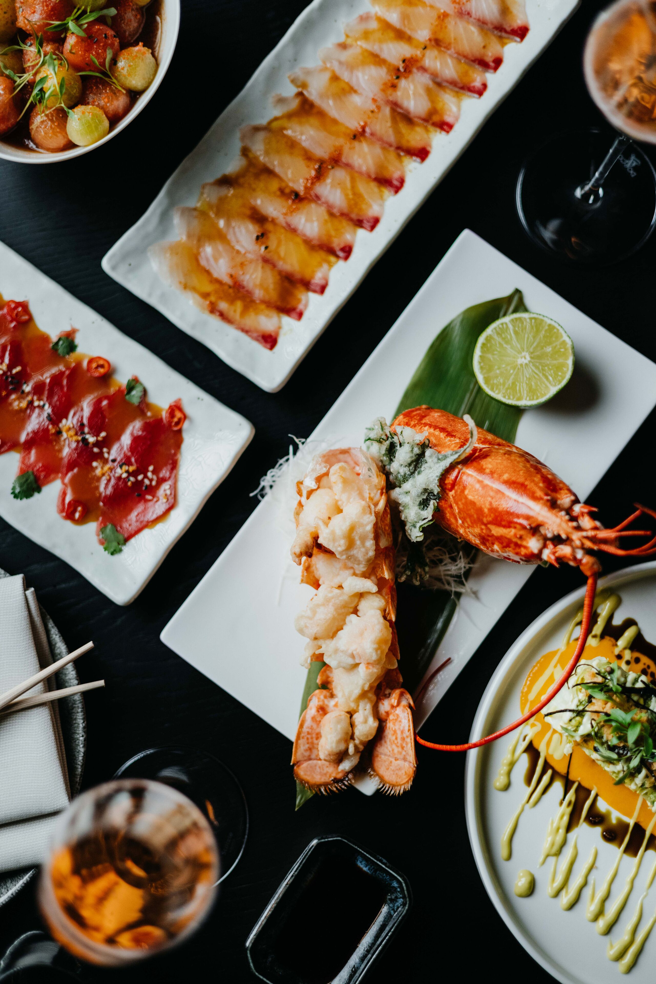 Variedad de platos de mariscos en platos blancos, incluyendo sashimi, un langostino y otras preparaciones de mariscos.