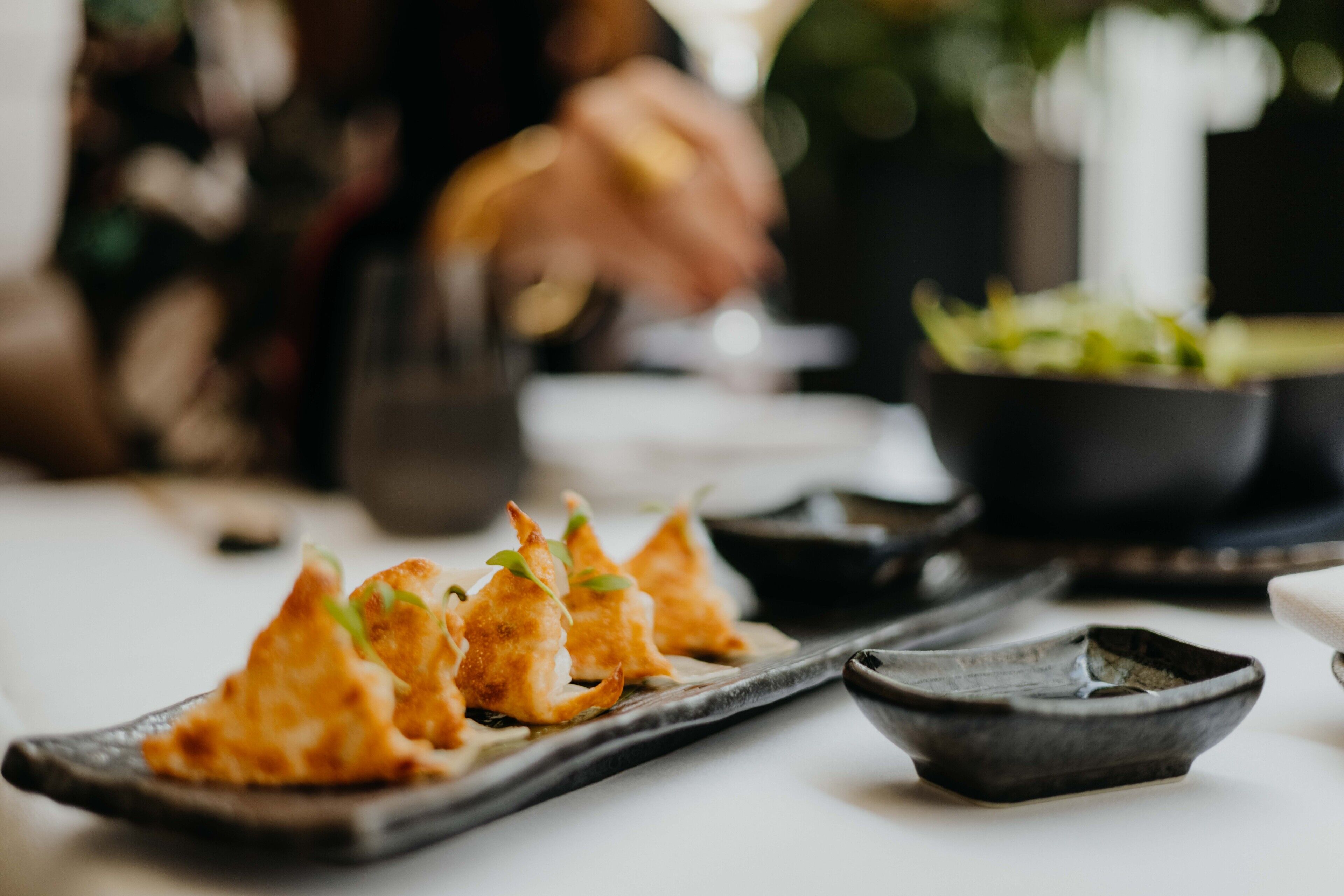 Une table à manger avec une assiette remplie de petites bouchées dorées et croustillantes, un petit bol de garniture verte et un bol noir.