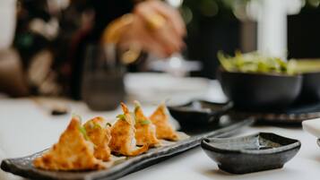 Une table à manger avec une assiette remplie de petites bouchées dorées et croustillantes, un petit bol de garniture verte et un bol noir.