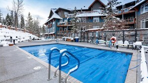 Ein Poolbereich mit klarem, blauem Pool, umgeben von Gebäuden mit Balkonen und einer verschneiten Landschaft.