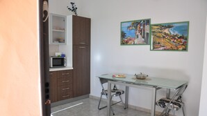 A compact kitchen with a microwave, cabinets, and a glass-top table. - Sa Teria Village - apartment 2 (tertenia)
