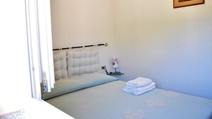 Een slaapkamer met een bed, een bedlampje, een lijst met een afbeelding aan de muur en een stapengevouwen handdoeken.