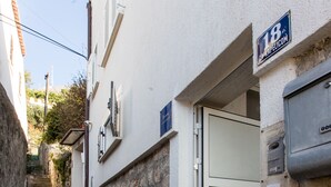 Un escalier étroit en pierre mène à un bâtiment blanc doté d’une porte en métal et d’une enseigne indiquant le numéro 18.