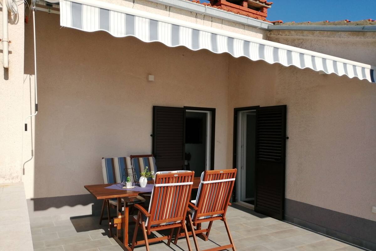 A patio with a table and two chairs, a tiled floor, and a building with a corrugated awning.