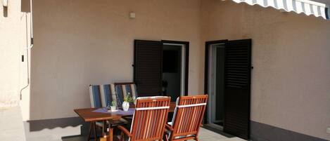 A patio with a table and two chairs, a tiled floor, and a building with a corrugated awning.