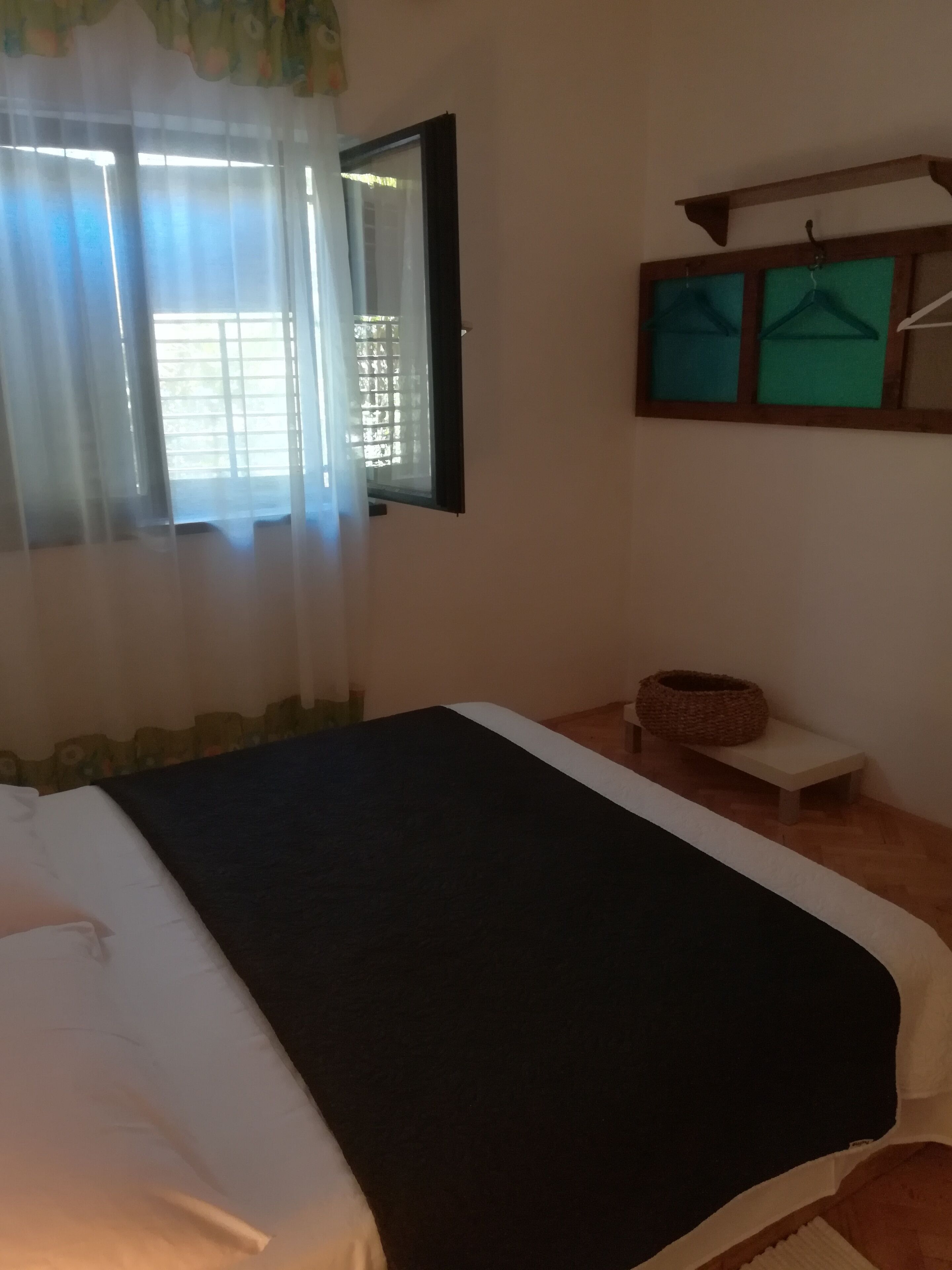 A bedroom with a bed, a bench, a basket, and a window with curtains.
