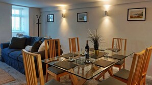 Un coin repas avec une table en verre, des chaises en bois et une bouteille de vin.