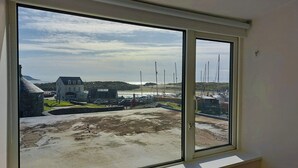 Une vue depuis une fenêtre donnant sur une zone côtière, avec un bâtiment, des bateaux et une plage de sable.
