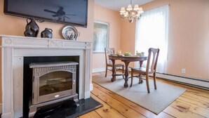 Ein Wohnzimmer mit Kamin, einem darüber angebrachten Fernseher, einem Esstisch mit Stühlen und einer Chandelüster.