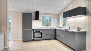 A modern kitchen with grey cabinets, a built-in oven, a window with a view of greenery, and a sink with a faucet.