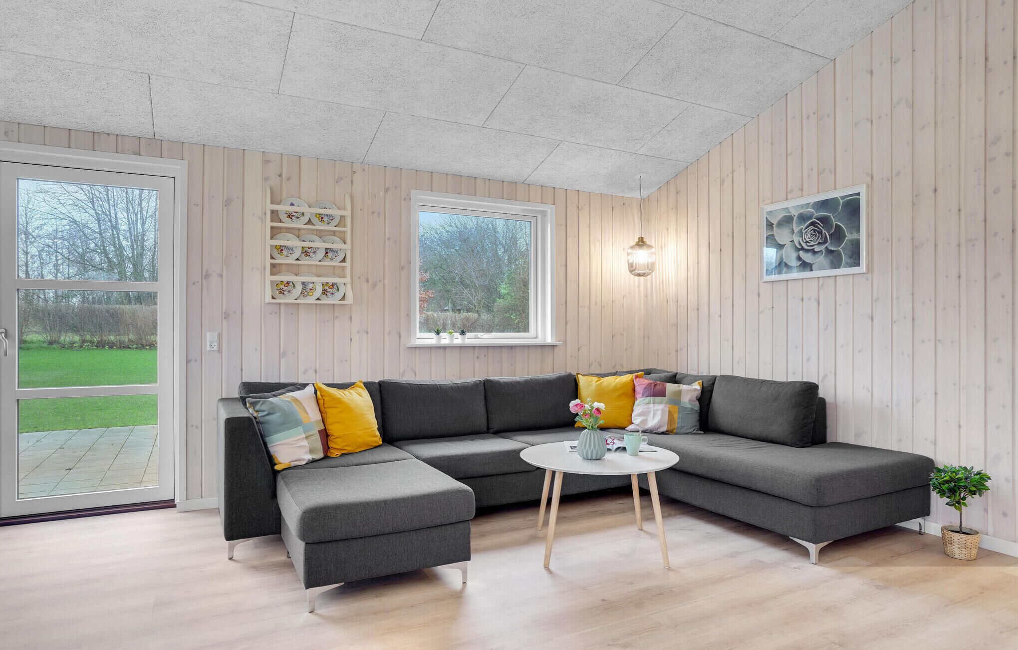 Ein modernes Wohnzimmer mit einem grauen Ecksofa, einem kleinen runden Couchtisch und einem Topf mit Pflanze.