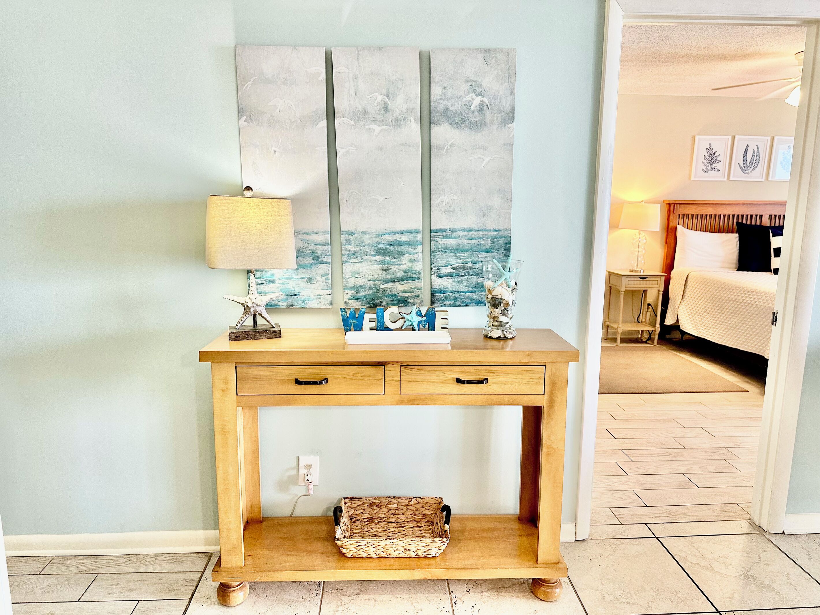 Een houten console tafel met een lamp, decoratieve objecten en een schilderij van meeuwen.