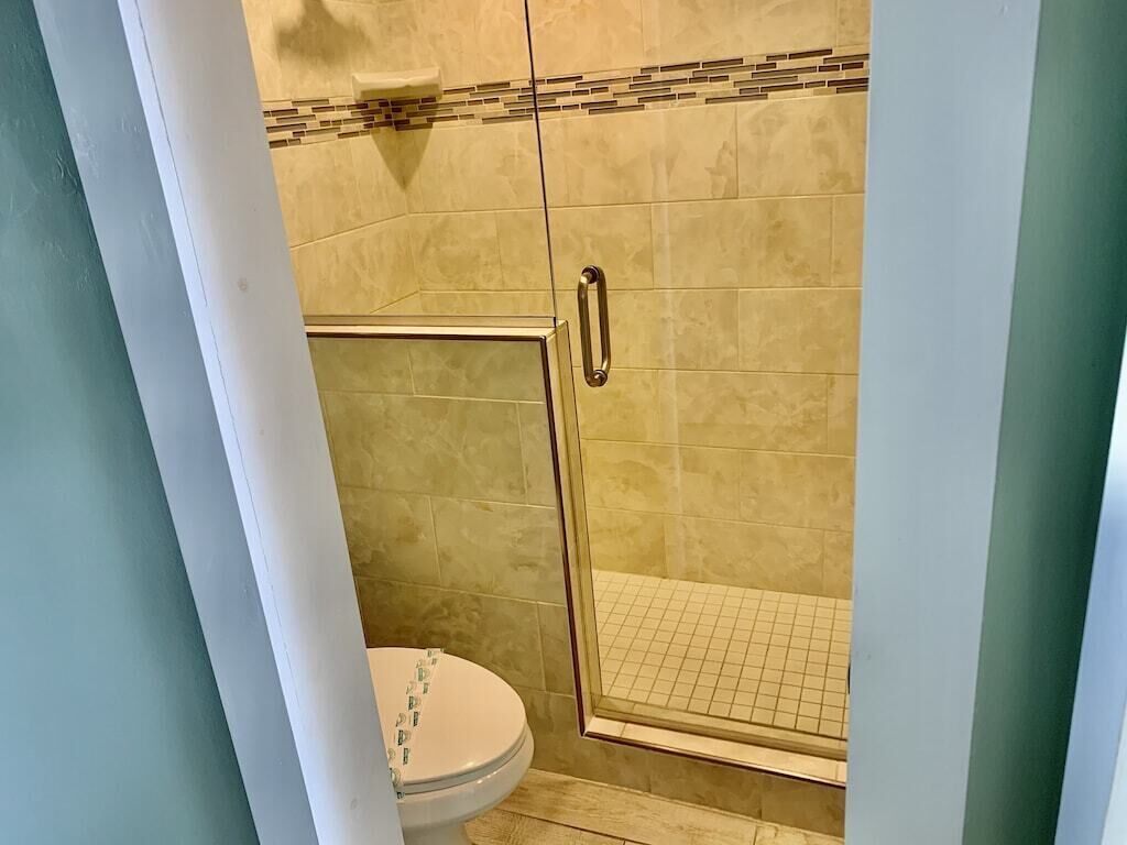 Un bagno con box doccia in vetro, un water e pareti rivestite di piastrelle beige.