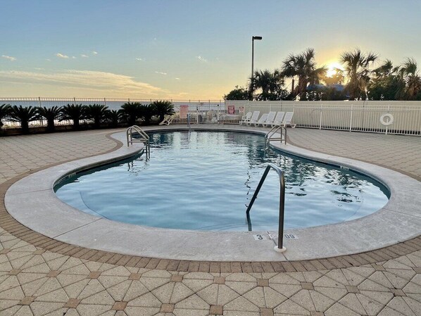 Uma piscina com deck ladrilhado, escada de metal e espreguiçadeiras.
