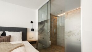Een moderne slaapkamer met een groot bed, een nachtkastje en een douchecabine met glazen wanden.