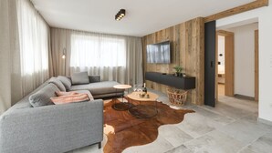 Een moderne woonkamer met een bank, een salontafel en een televisie die aan een houten wand is bevestigd.