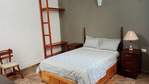 Ein Schlafzimmer mit einem Holzbett, einem Nachttisch, einem Beistelltisch, einem Stuhl und einer an der Wand stehenden Leiter.