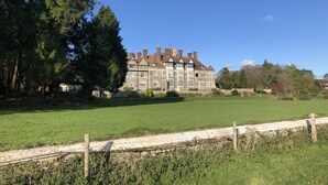 Un grand bâtiment historique, doté de nombreuses cheminées et d’une pelouse bien entretenue à l’avant.