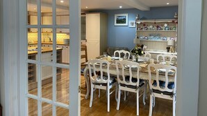 Un coin repas avec une table en bois, des chaises blanches et une cuisine en arrière-plan.