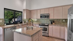 A modern kitchen with a built-in dishwasher, stainless steel appliances, and a large window offering a view of greenery. - PGA Condo with Gorgeous View of Mountains and Fairway (La Quinta)