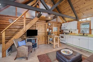 A cozy log cabin interior with a living area, a kitchen, and a dining space. - Nature's Nook - Fire Pit & Near Fishing & Golf (Eagle Rock)
