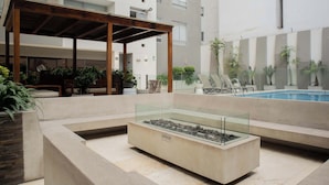 A modern outdoor pool area with a glass-enclosed water feature, lounge seating, and a wooden pergola.