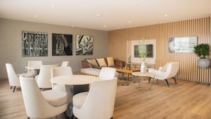 A modern lounge area with a sofa, chairs, and a coffee table. There are wall art pieces and a potted plant.