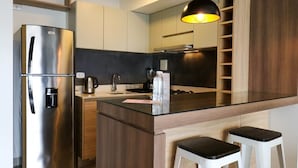 A modern kitchen with a stainless steel refrigerator, a coffee maker, and a black pendant light.