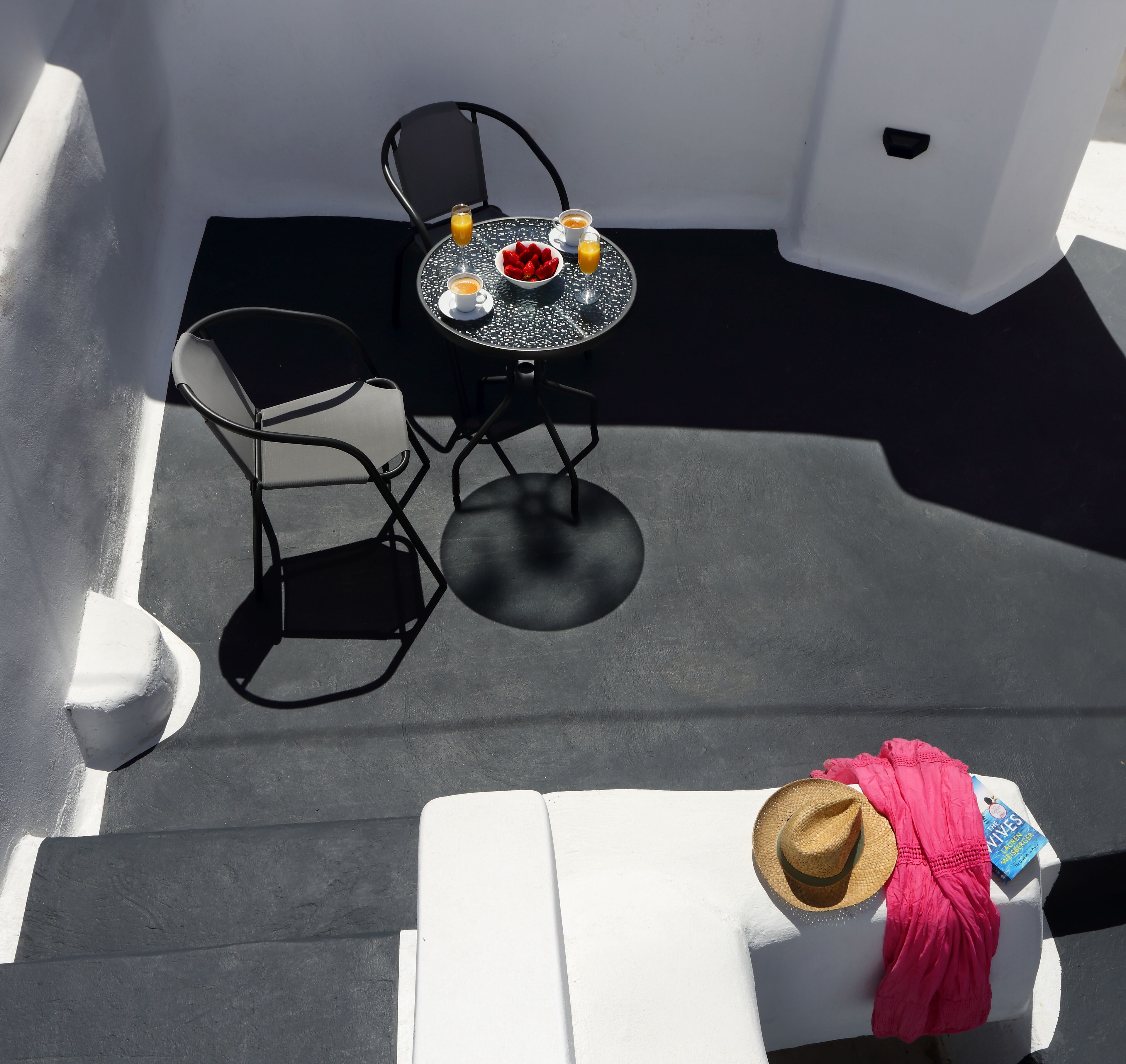 Een klein terras met een tafel en stoelen, een witte stoel met een hoed en handdoek, en een waterfles.