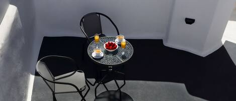 Een klein terras met een tafel en stoelen, een witte stoel met een hoed en handdoek, en een waterfles.
