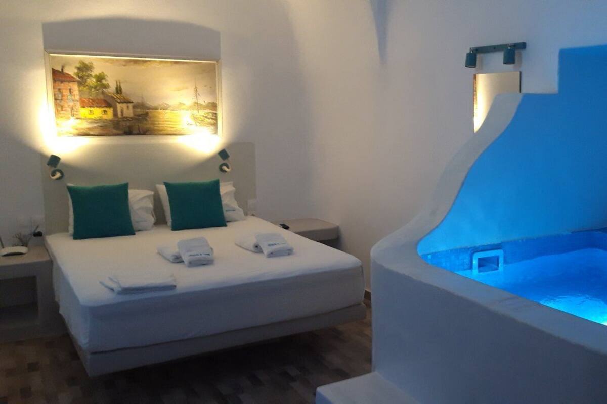 A hotel room with a bed, a painting, a nightstand, and a blue-lit bathtub.