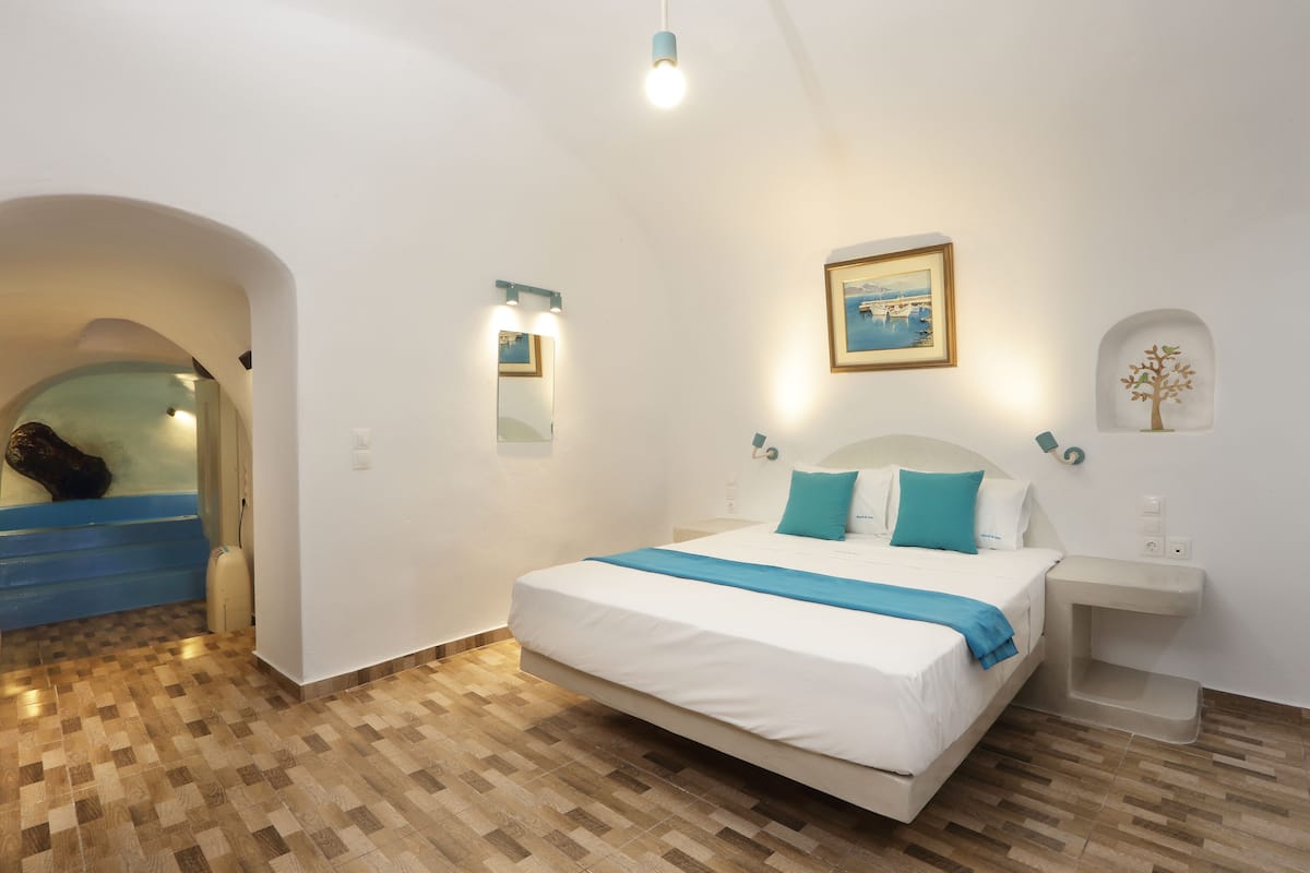A bedroom with a bed, a bedside table, a wall-mounted light, a framed picture, and a small shelf with a decorative item.