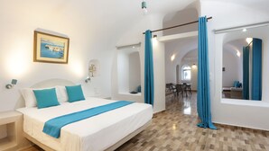 Ein Hotelzimmer mit einem großen Bett, einem kleinen Tisch, einem Sessel, einem Fenster mit Vorhängen und Blick ins Innere.
