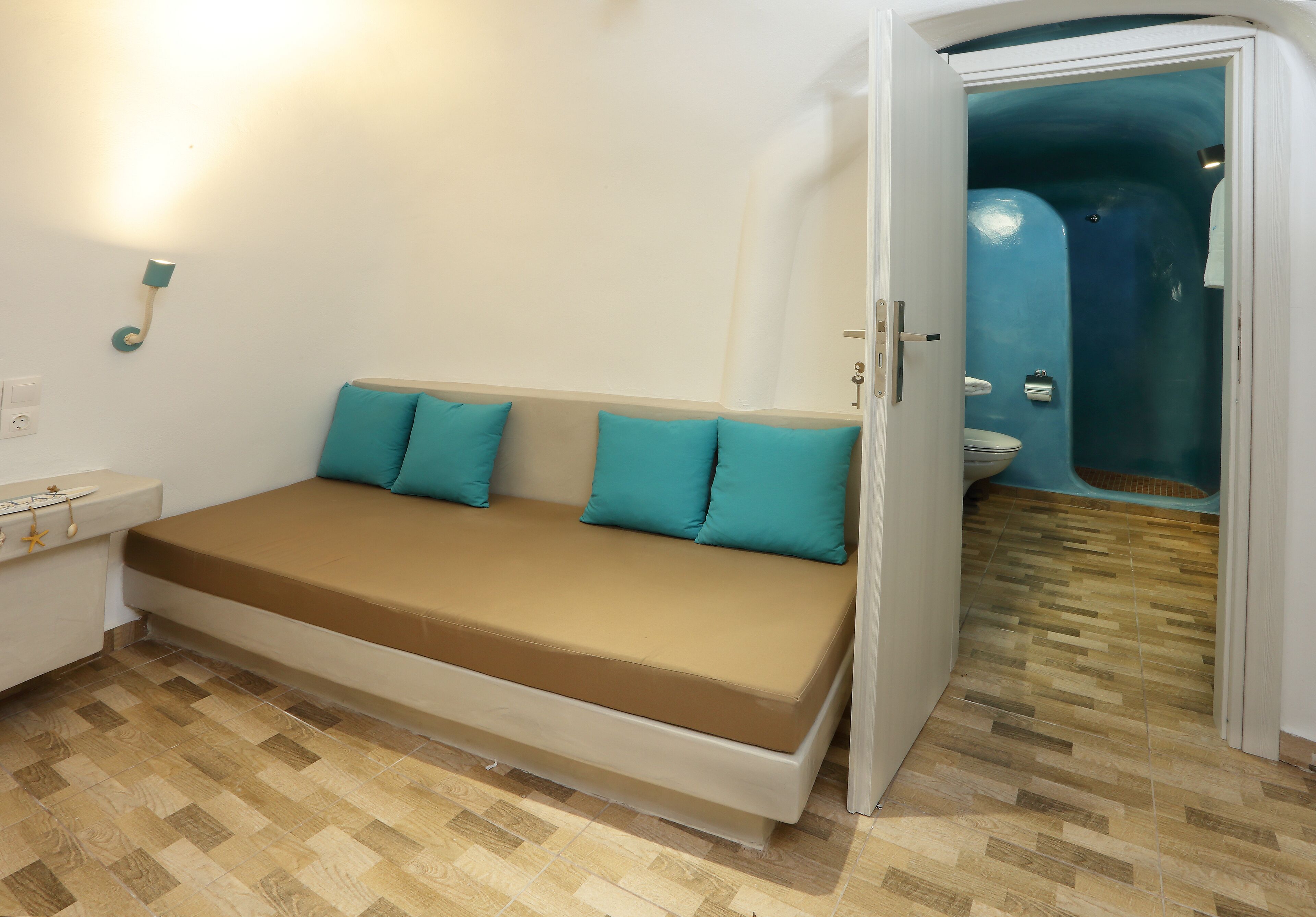 Quarto com sofá-cama, uma pequena mesa de cabeceira e um banheiro visível por uma porta aberta.