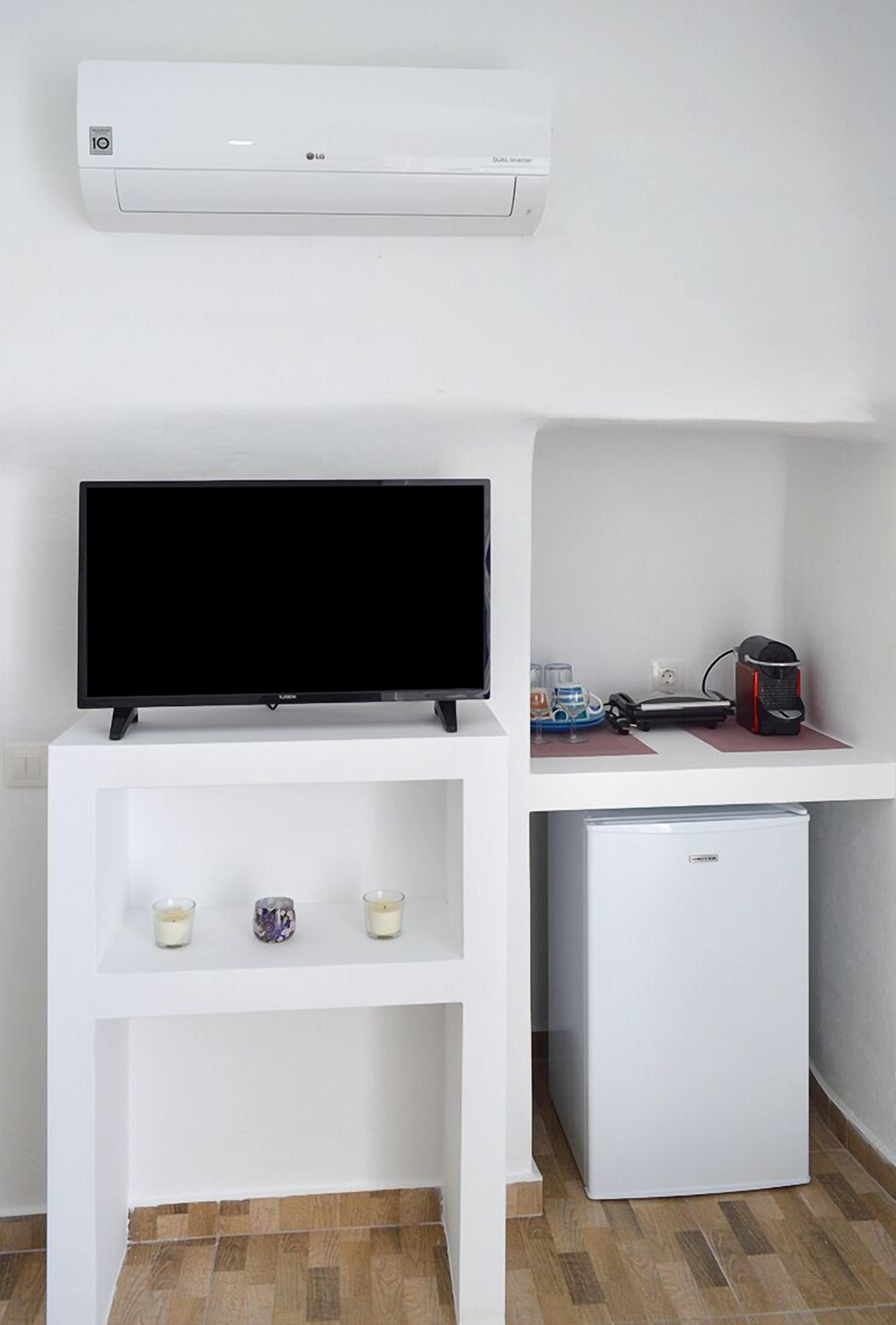 Un mueble blanco de entretenimiento con un televisor de pantalla plana, un refrigerador pequeño y un estante con velas.