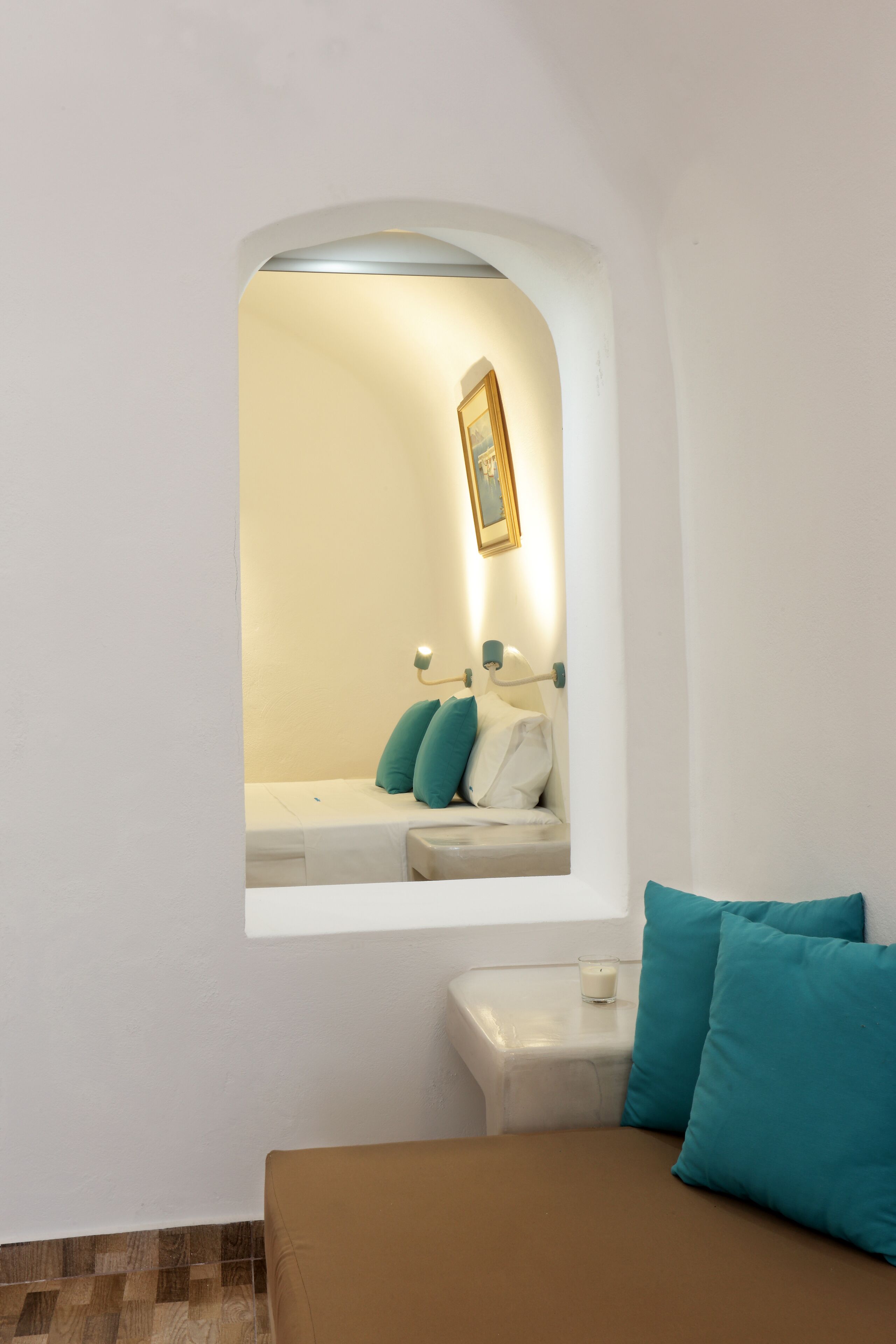 Quarto com cama, uma mesinha e janela com vista para um banheiro.
