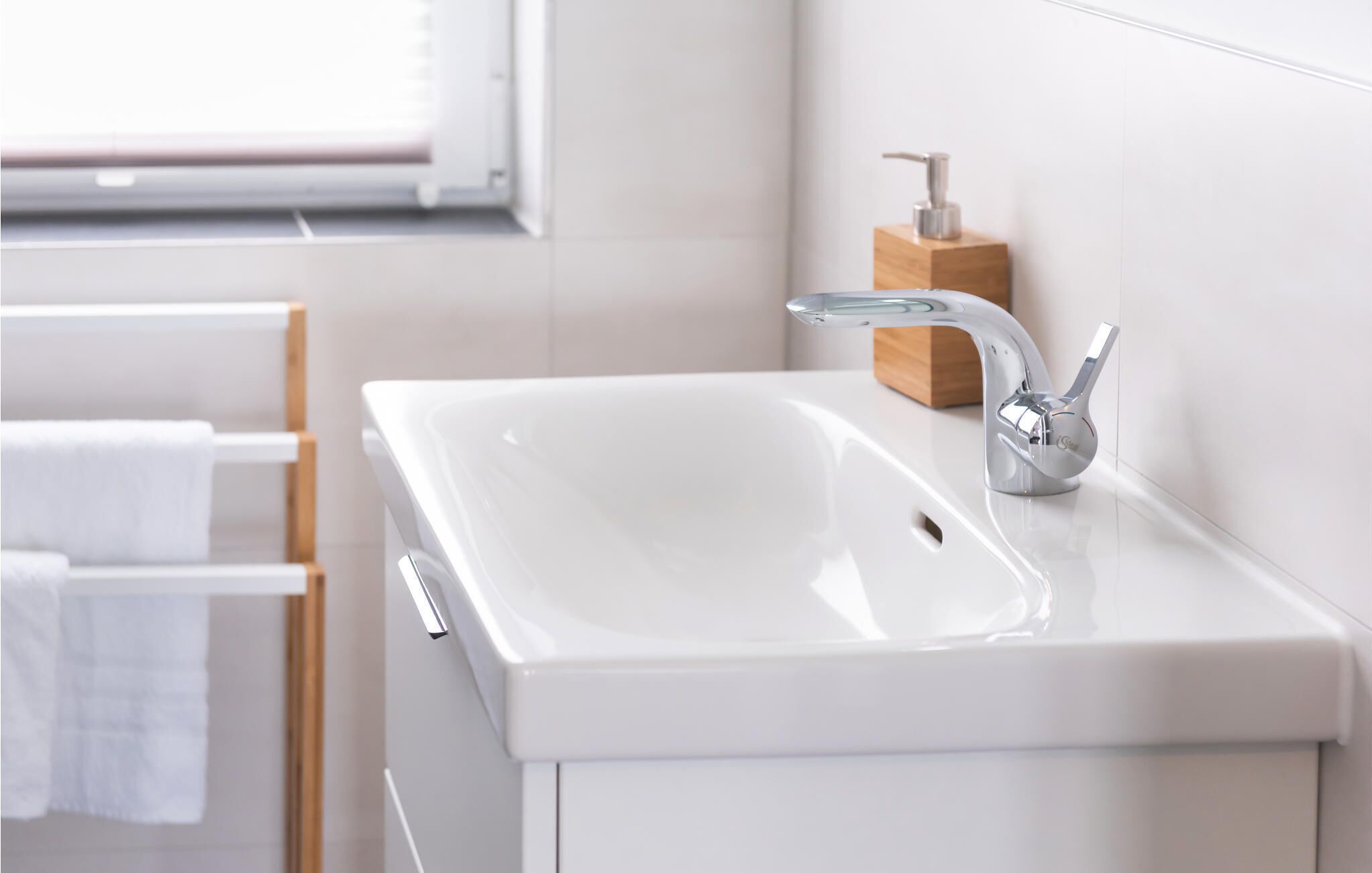 Een moderne badkamer met een wit wastafeltje, een chromen kraan en een houten zeepdispenser.