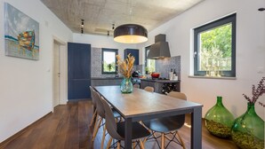 A modern kitchen with a dining area, featuring a large island, dark cabinetry, and a view through a window. - Modern Villa Leonardo with an outdoor pool (Porec)