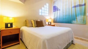 A hotel room with a bed, two bedside tables with lamps, a window with blinds, and a large abstract painting on the wall. - Castillito del Caribe 4 Bedrooms (Isla Mujeres)