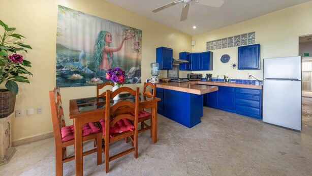 A kitchen with blue cabinets, a dining table with chairs, a ceiling fan, and a painting on the wall. - Castillito del Caribe 4 Bedrooms (Isla Mujeres)